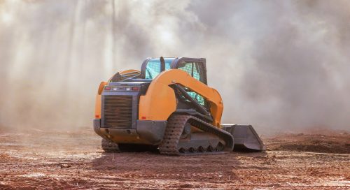 Compact bulldozer machinery is working on construction site, stirring up dust during earth moving is land preparation site development.